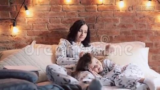 母女俩穿着睡衣坐在床上，一起看电视。 家庭时间视频