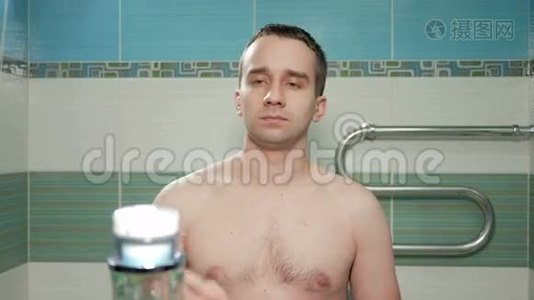 在旅馆房间的浴室里，一个年轻迷人的男人在她的脸上涂上了奶油。他看着镜头，轻轻地视频