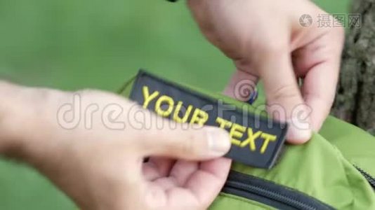 在绿色的背包上贴上一个补丁，上面写着你的文字。 黑色背景上的黄色字母视频