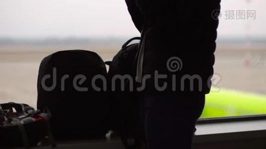 一名年轻女子在机场的一扇大窗户前用智能手机慢镜头视频