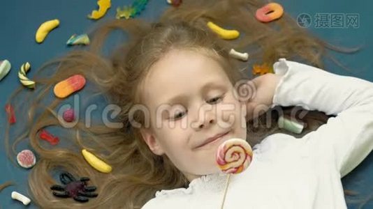 带棒棒糖的小女孩躺在蓝色的背景上。 特写肖像，俯视图视频