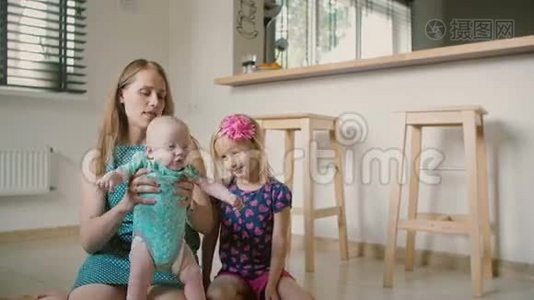 漂亮的年轻妈妈和她的小儿子和可爱的小女儿坐在厨房的地板上。 慢动作视频