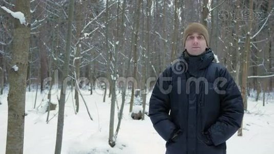 年轻人看着镜头，在冬天的森林里微笑。 冰雪景观。 一个穿深色夹克和暖帽的男人视频