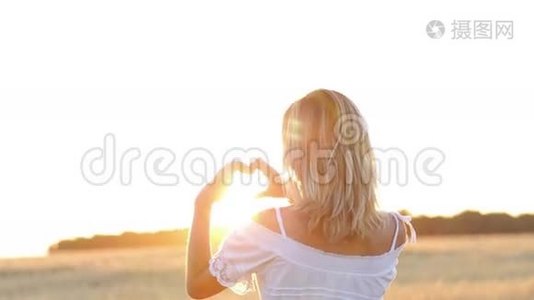 美丽的女孩用她的双手在大自然日落的背景下做着心。视频