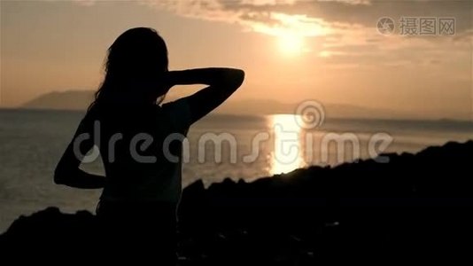 美丽的年轻女性在夕阳下仰望大海和举起双手的剪影视频