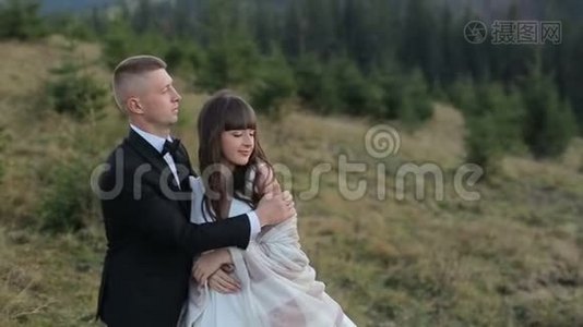 年轻漂亮的新婚夫妇在日落时一起在山坡上。 可爱的新郎和新娘。 风视频