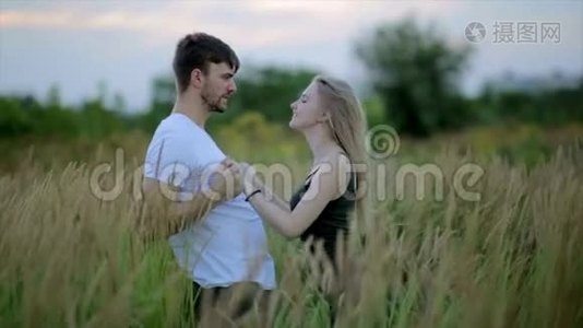 一对相爱的夫妻，一个男人亲吻一个美丽的年轻女子，并在日落或日出时把她举起来和她一起在田野上跳舞视频