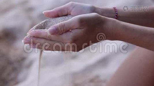 靠近女孩的手，白色的沙子过滤她的手指，而坐在海滩上。 印度尼西亚巴厘视频