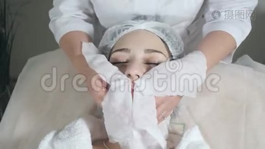 用无菌餐巾纸脸擦拭.. 年轻漂亮的女人在美容院接受治疗。 面部清洁泡沫使用。视频