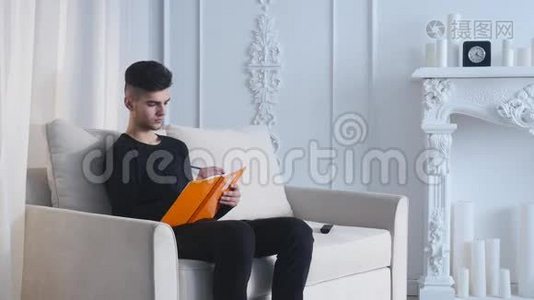 一个英俊的年轻人坐在沙发上，在家写笔记本视频