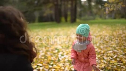 快乐的年轻妈妈和她的小女儿在秋天的公园里玩，妈妈和女孩扔树叶和笑。 慢慢慢慢视频