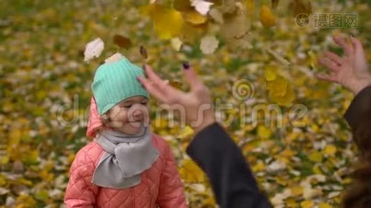 快乐的年轻妈妈和她的小女儿在秋天的公园里玩，妈妈和女孩扔树叶和笑。 慢慢慢慢视频