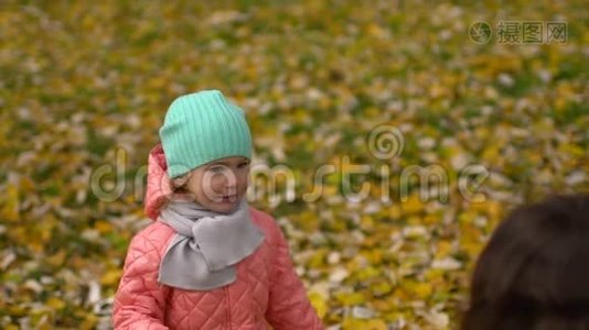 快乐的年轻妈妈和她的小女儿在秋天的公园里玩，妈妈和女孩扔树叶和笑。 慢慢慢慢视频