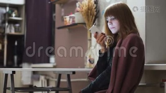 年轻漂亮的红发女郎在家里使用智能手机视频