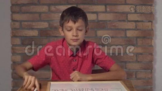 坐在办公桌前的孩子拿着一张挂图，背景红砖墙上有刻字的签名。视频