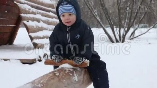 冬天的公园里下雪的时候，小可爱的男孩在木跷跷板上视频