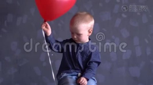 穿着蓝色衣服的滑稽男孩正在灰色的墙上玩红色的气球。 孩子在家很开心视频