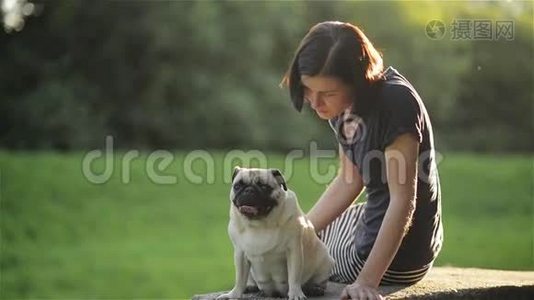 日落时，年轻漂亮的女孩在公园里抚摸她的狗。 女人玩她的狗，狗和主人坐在视频