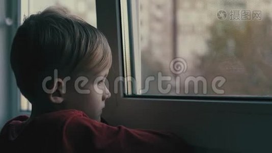 孩子悲伤而孤独地透过窗户看。 孩子很沮丧视频