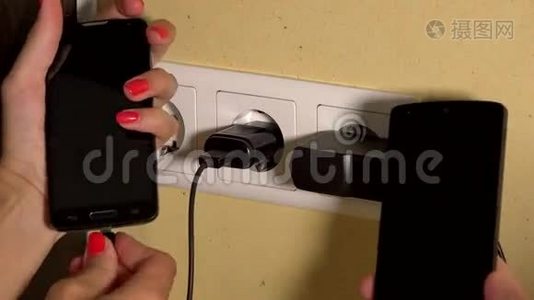 男人和女人手拿着充电智能手机连接到墙上插座。 特写视频