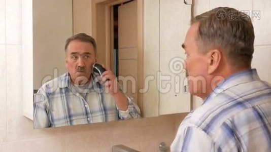 一个老人在浴室里刮电动剃须刀。 他照镜子，仔细地剃掉她所有的头发。 它的叶子视频