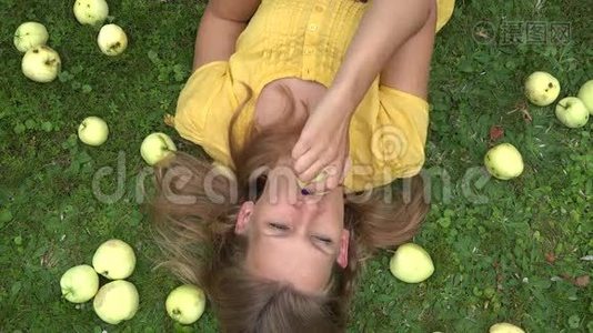 美丽微笑的年轻女子躺在草地上，咬着苹果水果。 4K视频