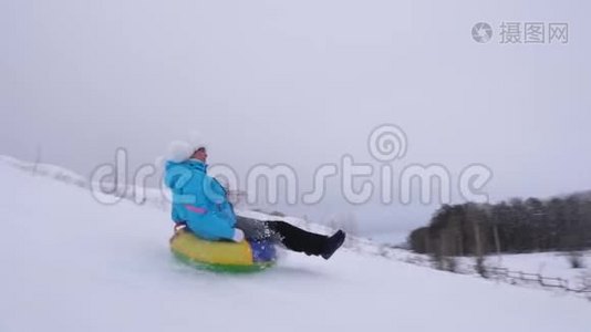 快乐的年轻女孩滑下雪滑到充气雪管上，挥动她的手。 女孩在公园里玩视频