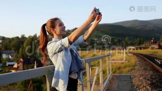 微笑着美丽的年轻女子在山上用智能手机拍照视频