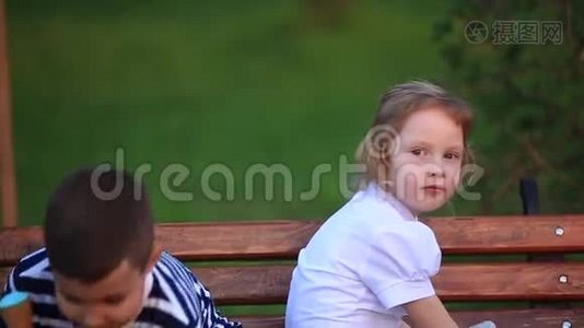 男孩吃冰淇淋，坐在长凳上，而女孩正在看。视频