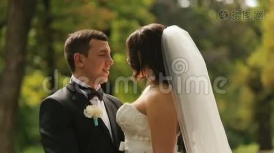 开朗刚结婚的新娘和新郎要接吻。 以夏季公园为背景的室外拍摄视频