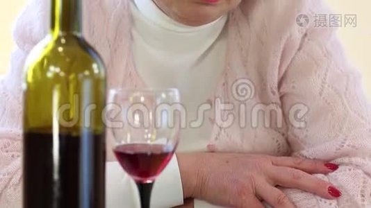 沮丧的高级妇女，桌上放着一瓶酒，看着摄像机视频