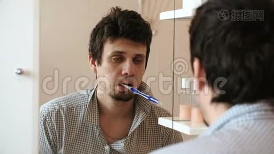 疲惫的困倦男人，一个宿醉的人，刚刚醒来，刷牙，看着他在镜子里的倒影。视频