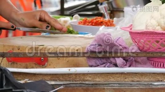 女人用一把大刀在厨房的木板上切绿色。 蔬菜和炊具旁边。 泰国街头食品视频