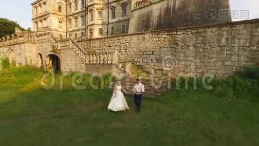 鸟瞰：美丽的婚礼情侣在古色古香的城堡前漫步.. 4k视频