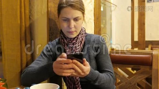 年轻的女人在手机上使用应用程序，喝咖啡，在咖啡馆里微笑。 4UHDK视频