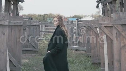 穿着黑色外套的漂亮女孩站在村庄围栏的背景下视频