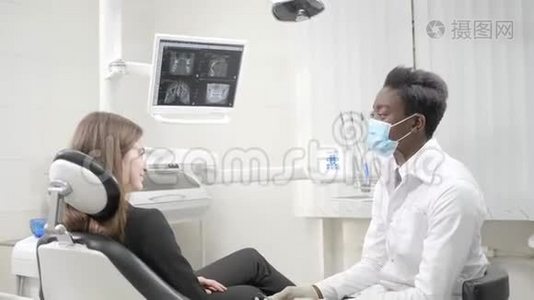 年轻的非裔美国男医生戴着医疗面具的牙医。 在牙科诊所的椅子上有个漂亮的女病人。 医药视频