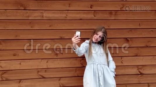 快乐的白种人少女在手机木制背景上自拍视频