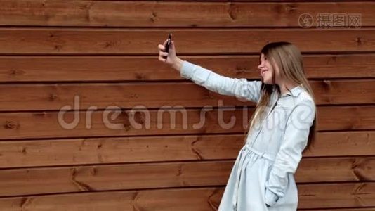快乐的白种人少女在手机木制背景上自拍视频