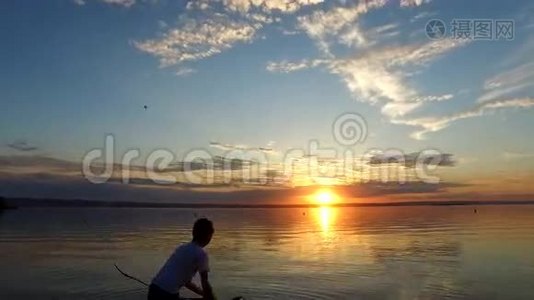 男孩少年被踢了一根长棍。 这个男孩站在一个大湖的岸边。 日落的夏夜视频