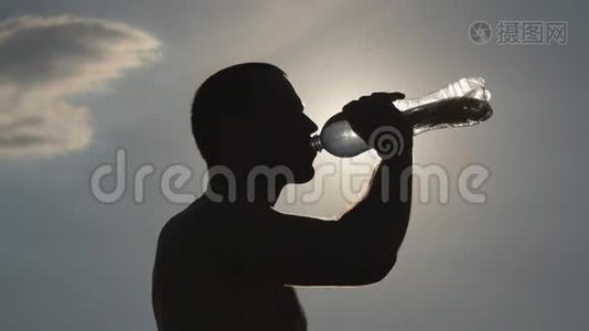 年轻人从自然界的塑料瓶里喝水。 日落时分有水的家伙。 背景中的太阳视频