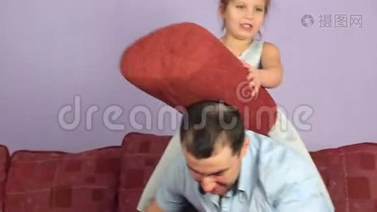 快乐的父亲和女儿在沙发上打枕头。视频