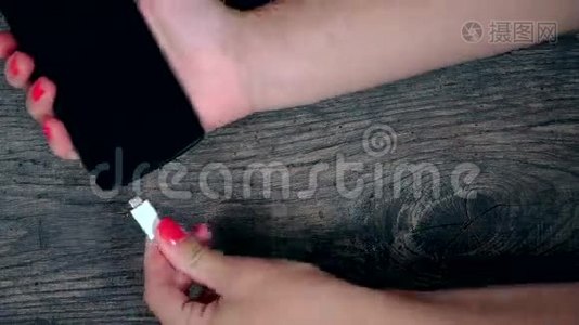 女性手连接白绳和黑色智能手机装置的木质背景视频