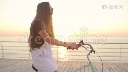年轻的美女骑着自行车在日落或日出的时候在海边玩得很开心视频