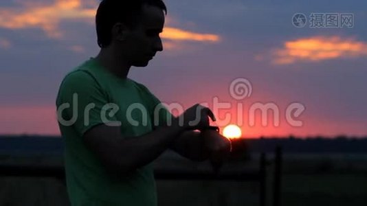 一个人在日落时看并触摸智能手表。 美丽的红天和树林后面的太阳视频