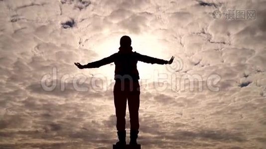 一个女孩站着的剪影像鸟一样举起双手飞向天空。视频
