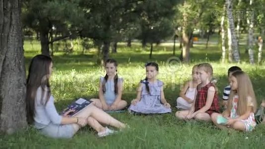 儿童和教育，年轻妇女在工作中，作为教育者向公园的男孩和女孩读书视频