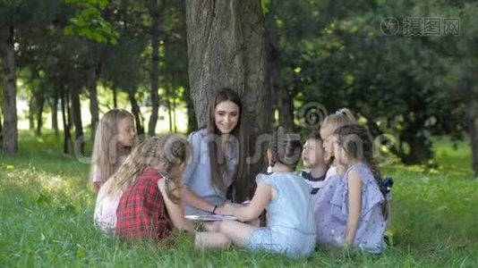 儿童和教育，年轻妇女在工作中，作为教育者向公园的男孩和女孩读书视频