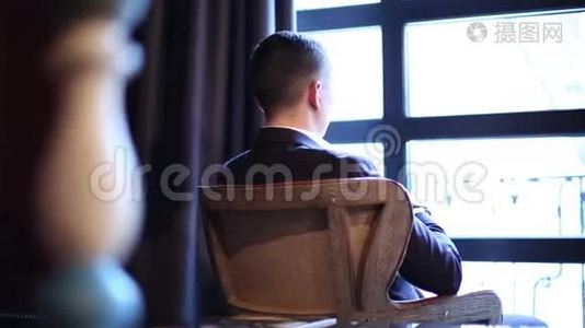 一个体贴的年轻人坐在窗前的复古扶手椅上。视频