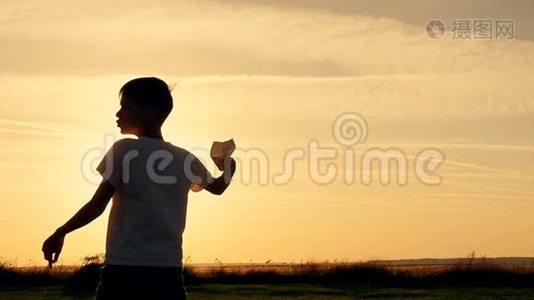 快乐的家伙在阳光下的田野里玩纸飞机。 日落时剪影视频